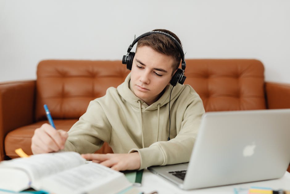 Teenage boy with headphones, focused on studying, using a laptop indoors