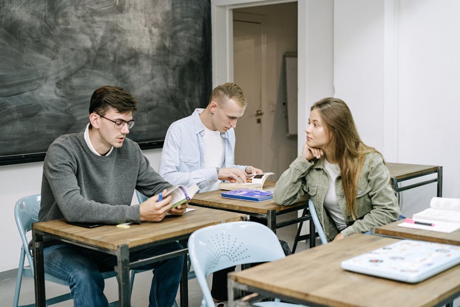 Group of young adults studying together in a classroom setting, engaged in reading and discussion.